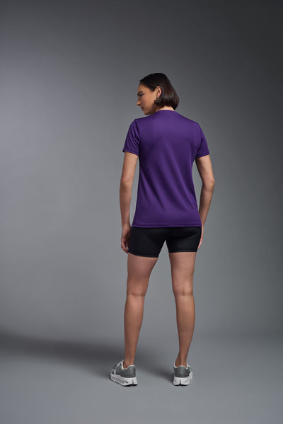 A female model with short brown hair on a gray background, wearing the Women's Oxymesh™ V-neck Tech Tee in the color dark purple from a full body back view. This shirt is made in the USA and is quick-drying and moisture-wicking. #color_dark-purple