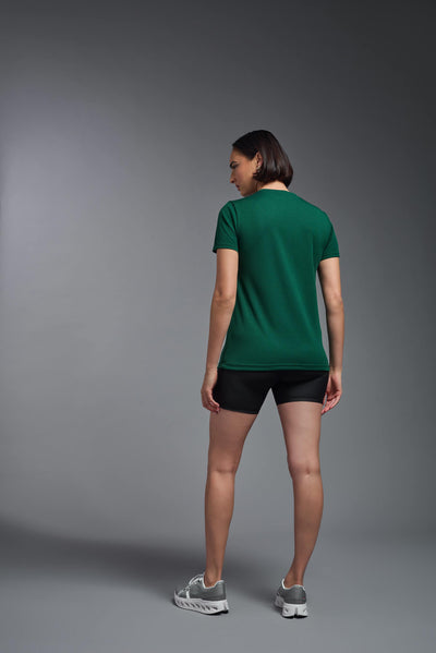 A female model with brown short hair on a gray background, wearing the Women's Oxymesh™ V-neck Tech Tee in the color forest green from a full body back view. This shirt is made in the USA and is quick-drying and moisture-wicking. #color_forest-green