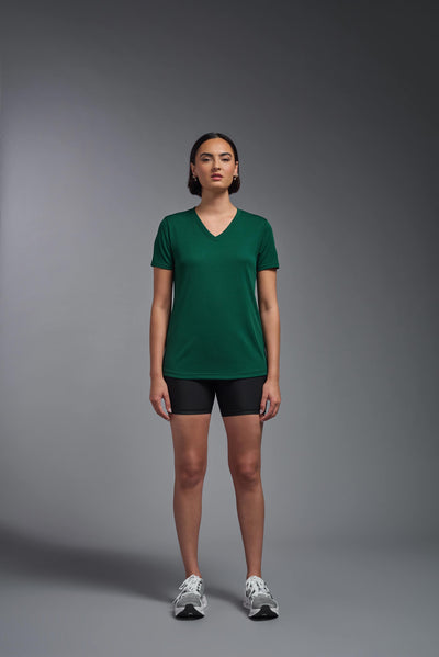 A female model with brown short hair on a gray background, wearing the Women's Oxymesh™ V-neck Tech Tee in the color forest green from a full body front view. This shirt is made in the USA and is quick-drying and moisture-wicking. #color_forest-green