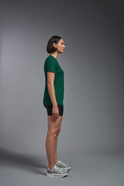 A female model with brown short hair on a gray background, wearing the Women's Oxymesh™ V-neck Tech Tee in the color forest green from a full body side view. This shirt is made in the USA and is quick-drying and moisture-wicking. #color_forest-green