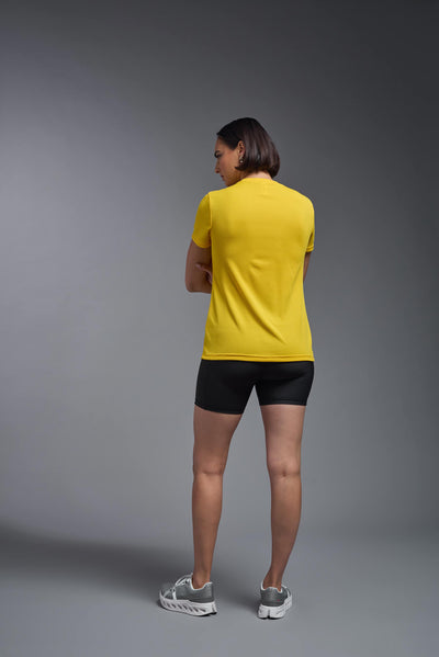 A female model with brown short hair on a gray background, wearing the Women's Oxymesh™ V-neck Tech Tee in the color gold from a full body back view. This shirt is made in the USA and is quick-drying and moisture-wicking. #color_gold