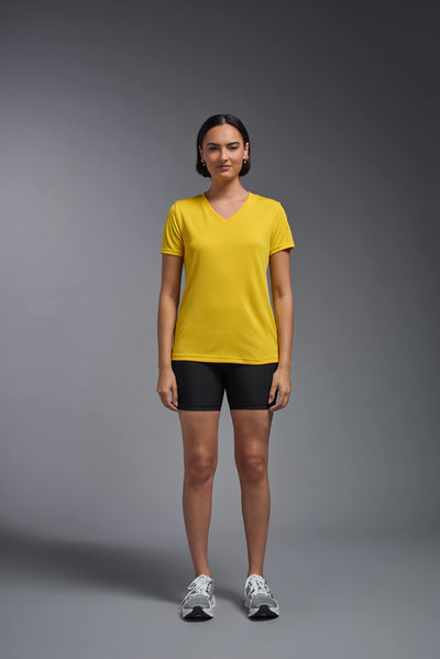A female model with brown short hair on a gray background, wearing the Women's Oxymesh™ V-neck Tech Tee in the color gold from a full body front view. This shirt is made in the USA and is quick-drying and moisture-wicking. #color_gold