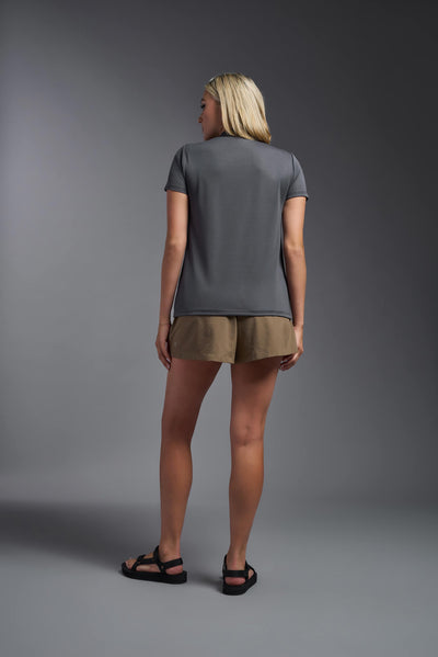 A blonde female model with long straight hair on a gray background, wearing the Women's Oxymesh™ V-neck Tech Tee in the color graphite from a full body back view. This shirt is made in the USA and is quick-drying and moisture-wicking. #color_graphite-gray