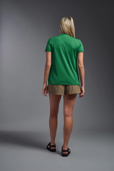A blonde female model with long straight hair on a gray background, wearing the Women's Oxymesh™ V-neck Tech Tee in the color kelly green from a full body back view. This shirt is made in the USA and is quick-drying and moisture-wicking. #color_kelly-green