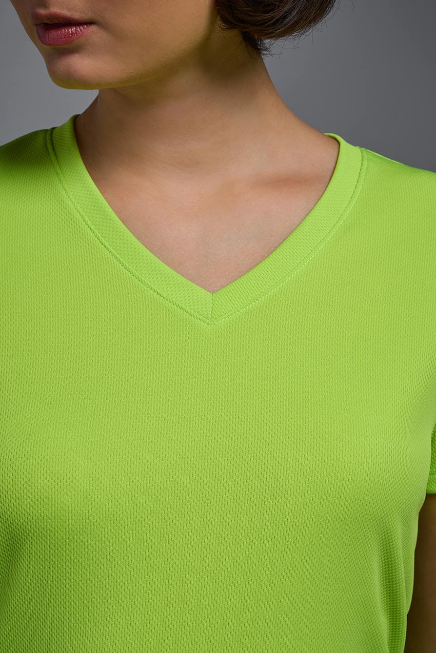 A female model with brown short hair on a gray background, wearing the Women's Oxymesh™ V-neck Tech Tee in the color key lime from a closeup collar front view. This shirt is made in the USA and is quick-drying and moisture-wicking. #color_key-lime