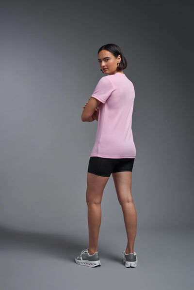 A female model with brown short hair on a gray background, wearing the Women's Oxymesh™ V-neck Tech Tee in the color pink from a full body back view. This shirt is made in the USA and is quick-drying and moisture-wicking. #color_pink