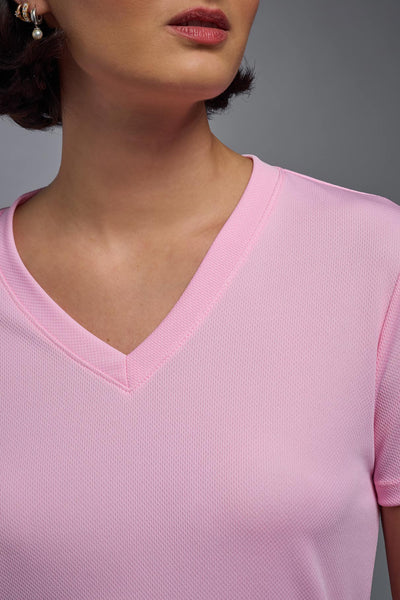 A female model with brown short hair on a gray background, wearing the Women's Oxymesh™ V-neck Tech Tee in the color pink from a closeup collar front view. This shirt is made in the USA and is quick-drying and moisture-wicking. #color_pink