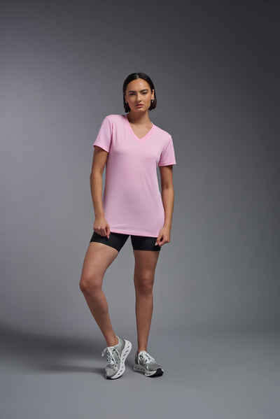 A female model with brown short hair on a gray background, wearing the Women's Oxymesh™ V-neck Tech Tee in the color pink from a full body front view. This shirt is made in the USA and is quick-drying and moisture-wicking. #color_pink