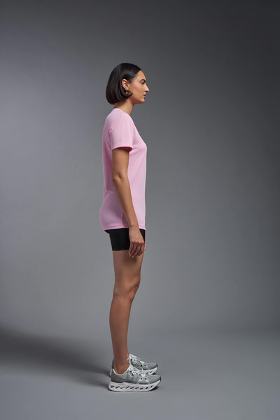 A female model with brown short hair on a gray background, wearing the Women's Oxymesh™ V-neck Tech Tee in the color pink from a full body side view. This shirt is made in the USA and is quick-drying and moisture-wicking. #color_pink