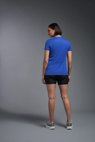 A female model with brown short hair on a gray background, wearing the Women's Oxymesh™ V-neck Tech Tee in the color royal blue from a full body back view. This shirt is made in the USA and is quick-drying and moisture-wicking. #color_royal-blue