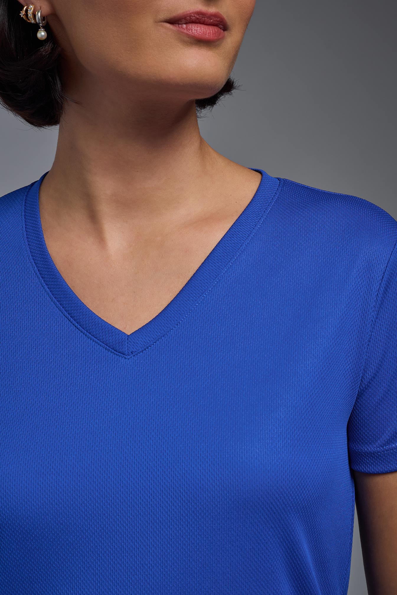 A female model with brown short hair on a gray background, wearing the Women's Oxymesh™ V-neck Tech Tee in the color royal blue from a closeup collar front view. This shirt is made in the USA and is quick-drying and moisture-wicking. #color_royal-blue