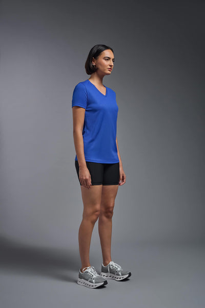 A female model with brown short hair on a gray background, wearing the Women's Oxymesh™ V-neck Tech Tee in the color royal blue from a full body side view. This shirt is made in the USA and is quick-drying and moisture-wicking. #color_royal-blue