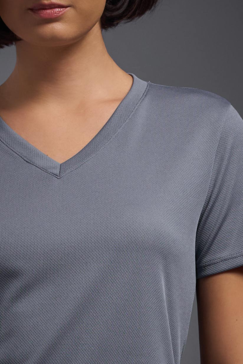 A female model with brown short hair on a gray background, wearing the Women's Oxymesh™ V-neck Tech Tee in the color steel gray from a closeup collar front view. This shirt is made in the USA and is quick-drying and moisture-wicking. #color_steel-gray