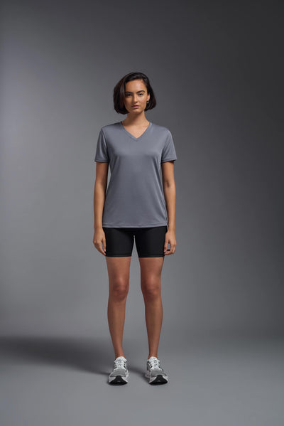 A female model with brown short hair on a gray background, wearing the Women's Oxymesh™ V-neck Tech Tee in the color steel gray from a full body front view. This shirt is made in the USA and is quick-drying and moisture-wicking. #color_steel-gray