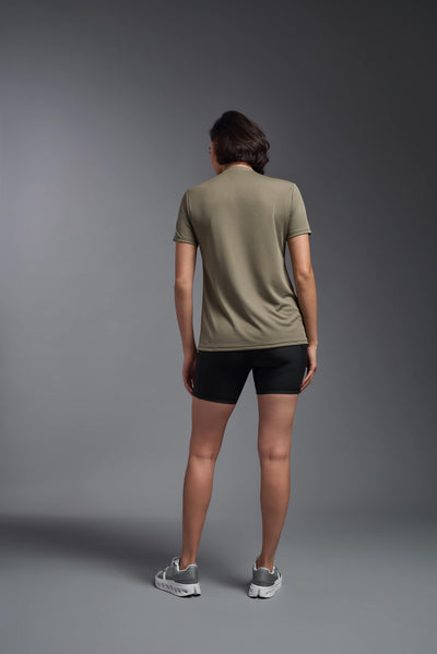 A female model with brown short hair on a gray background, wearing the Women's Oxymesh™ V-neck Tech Tee in the color tan-499 from a full body back view. This shirt is made in the USA and is quick-drying and moisture-wicking. #color_tan-499