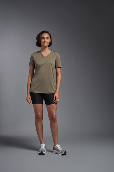 A female model with brown short hair on a gray background, wearing the Women's Oxymesh™ V-neck Tech Tee in the color tan-499 from a full body front view. This shirt is made in the USA and is quick-drying and moisture-wicking. #color_tan-499