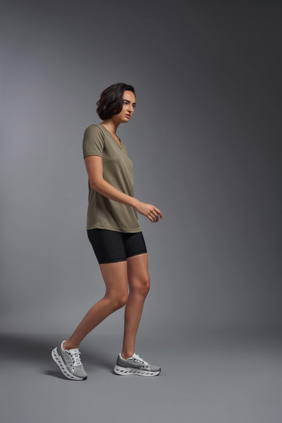 A female model with brown short hair on a gray background, wearing the Women's Oxymesh™ V-neck Tech Tee in the color tan-499 from a full body side view. This shirt is made in the USA and is quick-drying and moisture-wicking. #color_tan-499