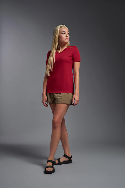 A blonde female model with long straight hair on a gray background, wearing the Women's Oxymesh™ V-neck Tech Tee in the color true red from a full body side view. This shirt is made in the USA and is quick-drying and moisture-wicking. #color_true-red