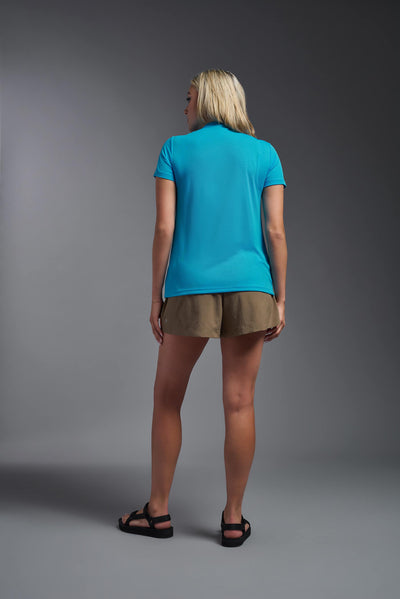 A blonde female model with long straight hair on a gray background, wearing the Women's Oxymesh™ V-neck Tech Tee in the color turquoise from a full body back view. This shirt is made in the USA and is quick-drying and moisture-wicking. #color_turquoise