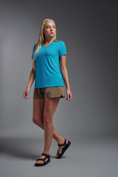 A blonde female model with long straight hair on a gray background, wearing the Women's Oxymesh™ V-neck Tech Tee in the color turquoise from a full body side view. This shirt is made in the USA and is quick-drying and moisture-wicking. #color_turquoise