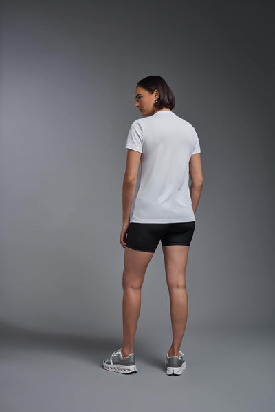 A female model with brown short hair on a gray background, wearing the Women's Oxymesh™ V-neck Tech Tee in the color white from a full body back view. This shirt is made in the USA and is quick-drying and moisture-wicking. #color_white