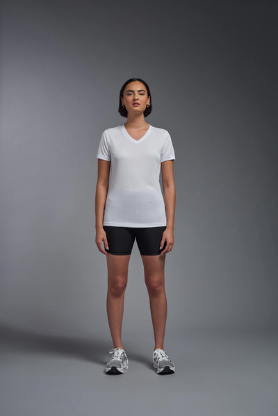 A female model with brown short hair on a gray background, wearing the Women's Oxymesh™ V-neck Tech Tee in the color white from a full body front view. This shirt is made in the USA and is quick-drying and moisture-wicking. #color_white
