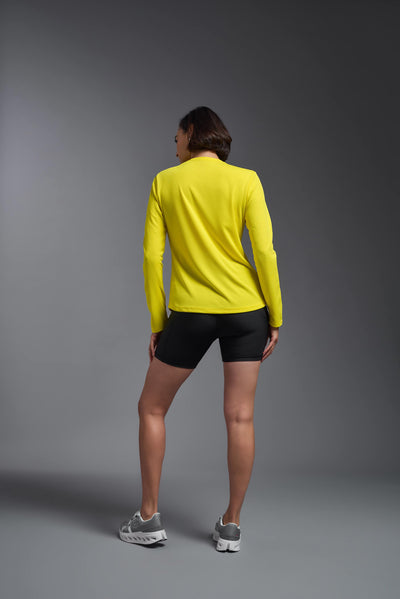 A female model with short brown hair on a gray background, wearing the Women's Oxymesh™ Long Sleeve Tech Tee in the color bright yellow from a full body back view. This shirt is made in the USA and is quick-drying and moisture-wicking. #color_bright-yellow