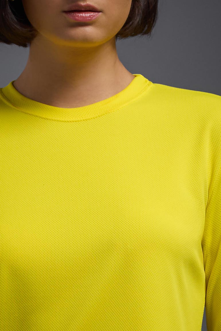 A female model with short brown hair on a gray background, wearing the Women's Oxymesh™ Long Sleeve Tech Tee in the color bright yellow from a closeup collar front view. This shirt is made in the USA and is quick-drying and moisture-wicking. #color_bright-yellow