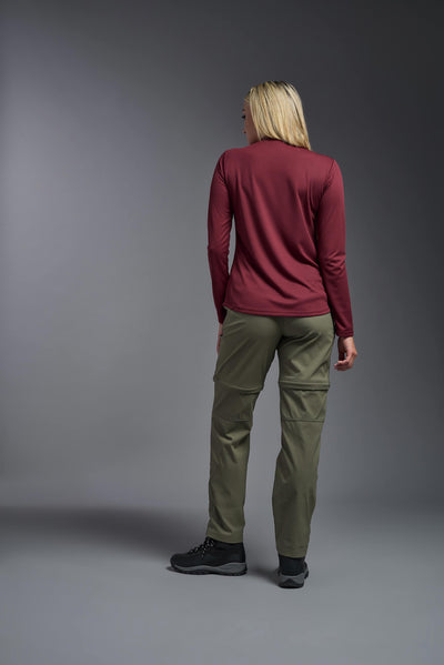 A blonde, female model with long straight hair on a gray background, wearing the Women's Oxymesh™ Long Sleeve Tech Tee in the color cardinal from a full body back view. This shirt is made in the USA and is quick-drying and moisture-wicking. #color_cardinal