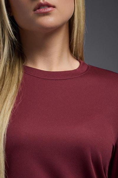 A blonde, female model with long straight hair on a gray background, wearing the Women's Oxymesh™ Long Sleeve Tech Tee in the color cardinal from a closeup collar front view. This shirt is made in the USA and is quick-drying and moisture-wicking. #color_cardinal