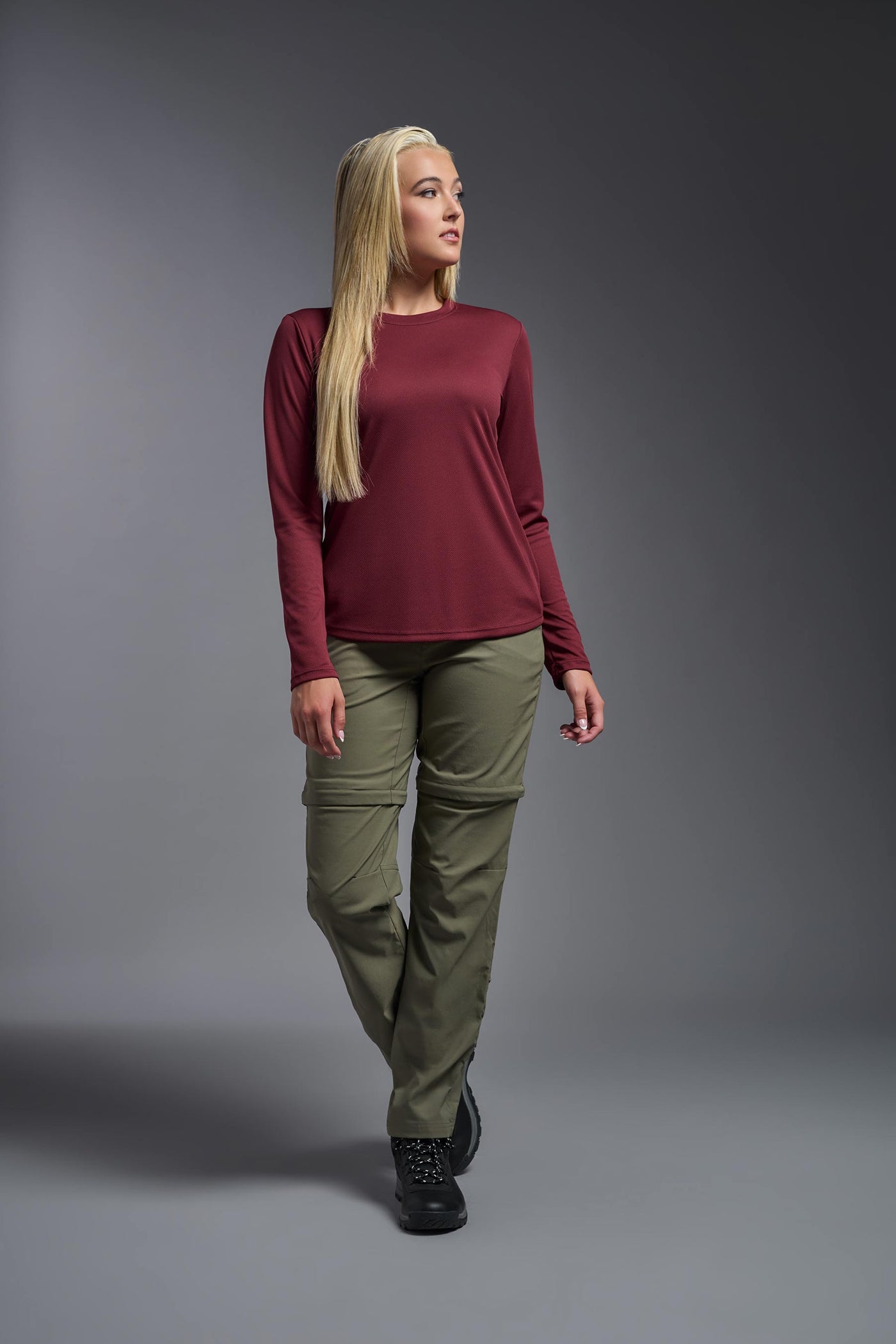 A blonde, female model with long straight hair on a gray background, wearing the Women's Oxymesh™ Long Sleeve Tech Tee in the color cardinal from a full body front view. This shirt is made in the USA and is quick-drying and moisture-wicking. #color_cardinal