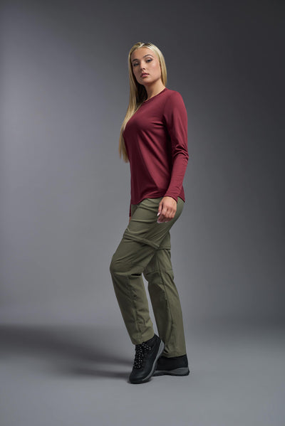 A blonde, female model with long straight hair on a gray background, wearing the Women's Oxymesh™ Long Sleeve Tech Tee in the color cardinal from a full body side view. This shirt is made in the USA and is quick-drying and moisture-wicking. #color_cardinal