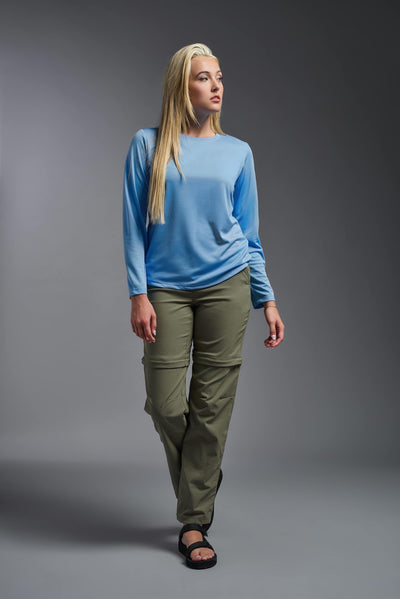 A blonde, female model with long straight hair on a gray background, wearing the Women's Oxymesh™ Long Sleeve Tech Tee in the color carolina blue from a full body front view. This shirt is made in the USA and is quick-drying and moisture-wicking. #color_carolina-blue