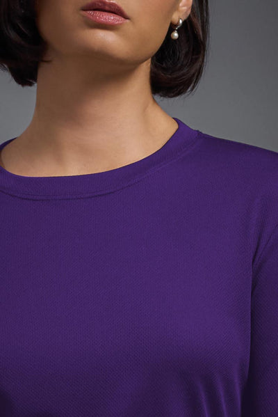 A female model with short brown hair on a gray background, wearing the Women's Oxymesh™ Long Sleeve Tech Tee in the color dark purple from a closeup collar view. This shirt is made in the USA and is quick-drying and moisture-wicking. #color_dark-purple