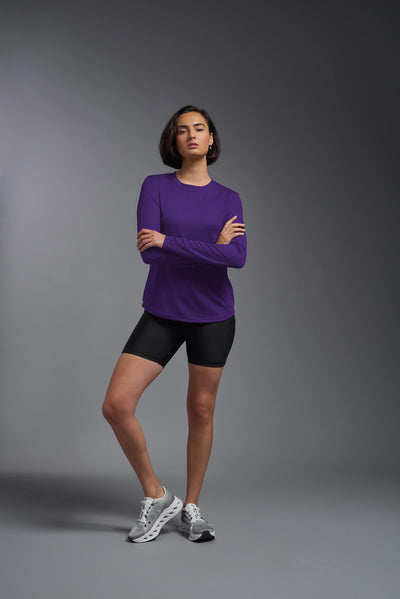 A female model with short brown hair on a gray background, wearing the Women's Oxymesh™ Long Sleeve Tech Tee in the color dark purple from a full body side view. This shirt is made in the USA and is quick-drying and moisture-wicking. #color_dark-purple