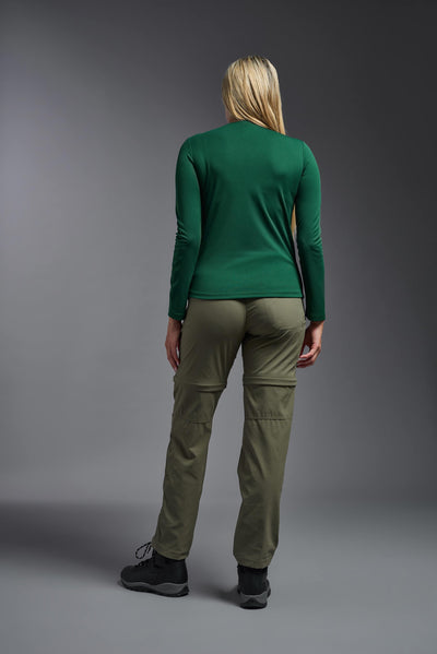 A blonde, female model with long straight hair on a gray background, wearing the Women's Oxymesh™ Long Sleeve Tech Tee in the color forest green from a full body back view. This shirt is made in the USA and is quick-drying and moisture-wicking. #color_forest-green