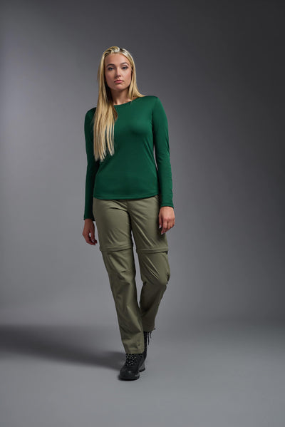 A blonde, female model with long straight hair on a gray background, wearing the Women's Oxymesh™ Long Sleeve Tech Tee in the color forest green from a full body front view. This shirt is made in the USA and is quick-drying and moisture-wicking. #color_forest-green