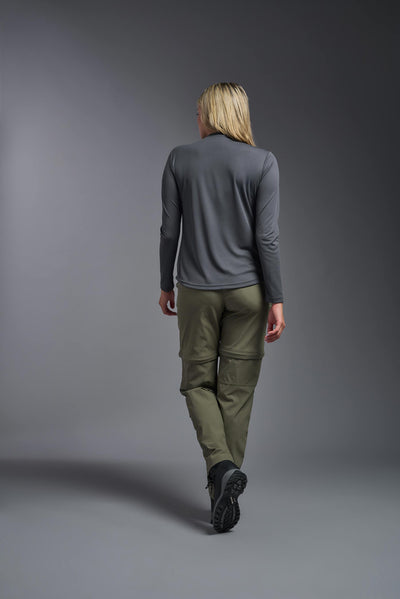 A blonde, female model with long straight hair on a gray background, wearing the Women's Oxymesh™ Long Sleeve Tech Tee in the color graphite gray from a full body back view. This shirt is made in the USA and is quick-drying and moisture-wicking. #color_graphite-gray