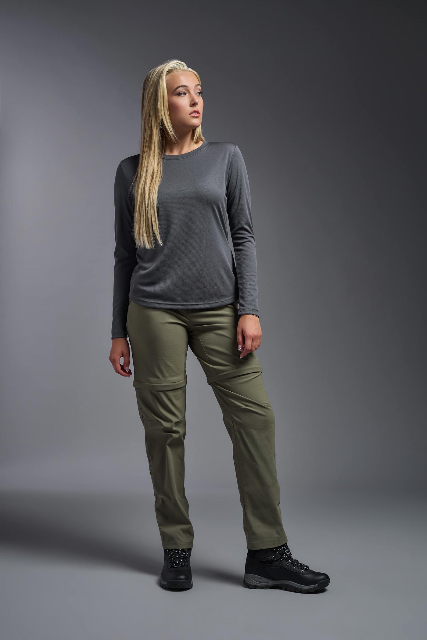 A blonde, female model with long straight hair on a gray background, wearing the Women's Oxymesh™ Long Sleeve Tech Tee in the color graphite gray from a full body front view. This shirt is made in the USA and is quick-drying and moisture-wicking. #color_graphite-gray