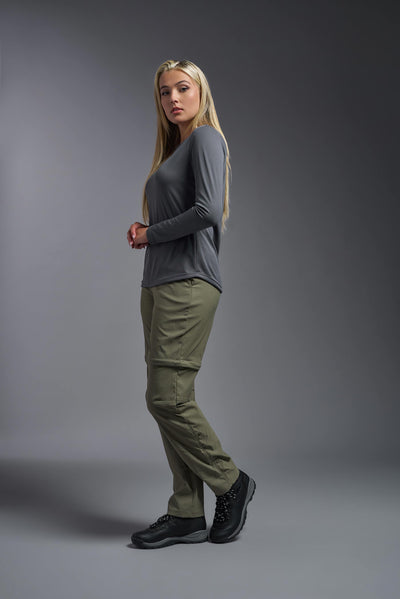 A blonde, female model with long straight hair on a gray background, wearing the Women's Oxymesh™ Long Sleeve Tech Tee in the color graphite gray from a full body side view. This shirt is made in the USA and is quick-drying and moisture-wicking. #color_graphite-gray