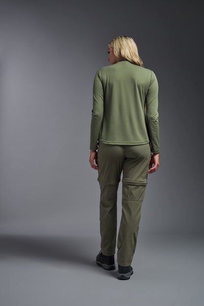 A blonde female model with long straight hair on a gray background, wearing the Women's Oxymesh™ Long Sleeve Tech Tee in the color military green from a full body back view. This shirt is made in the USA and is quick-drying and moisture-wicking. #color_military-green