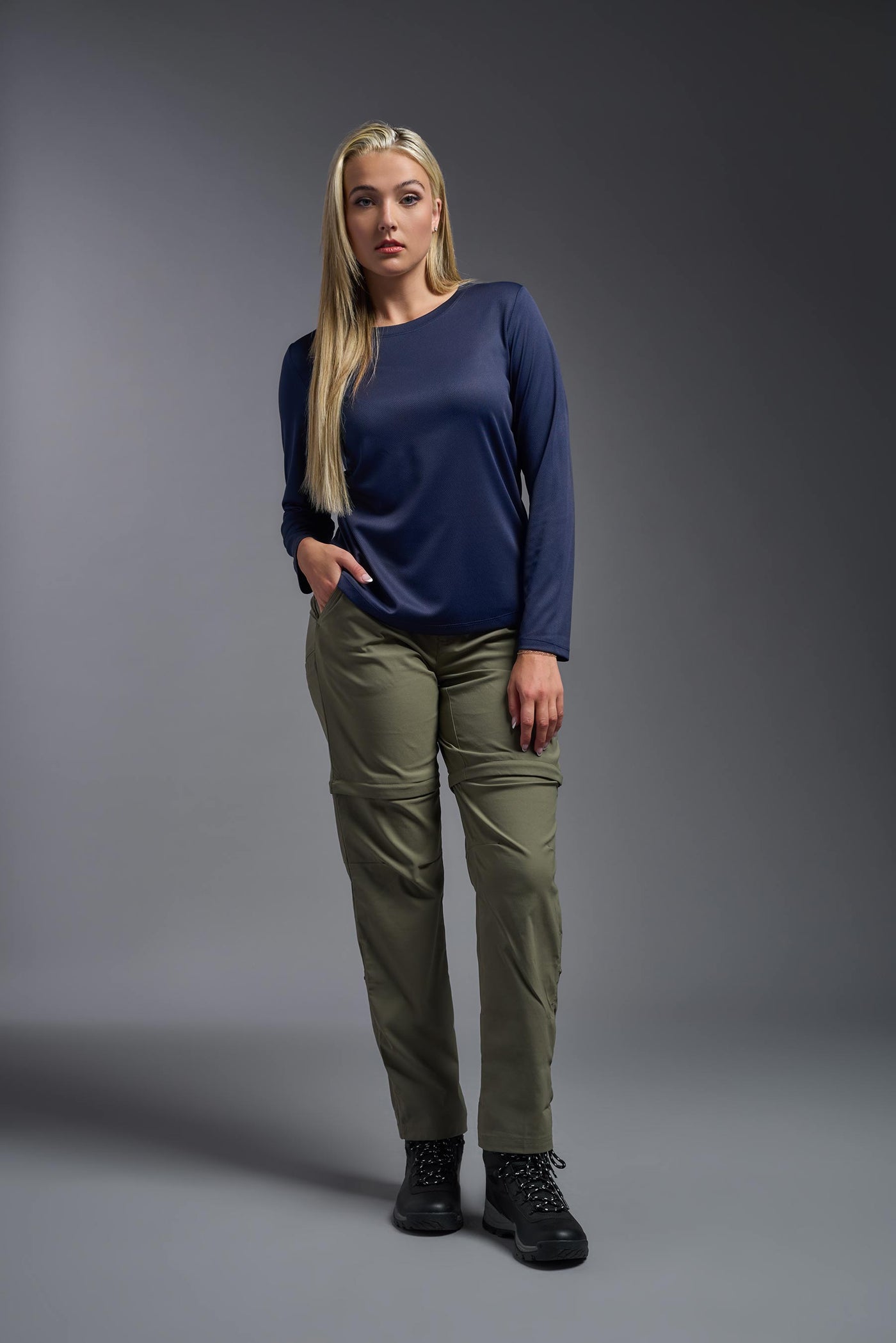 A blonde, female model with long straight hair on a gray background, wearing the Women's Oxymesh™ Long Sleeve Tech Tee in the color navy blue from a full body front view. This shirt is made in the USA and is quick-drying and moisture-wicking. #color_navy-blue