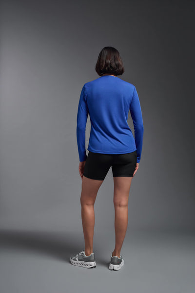 A female model with short brown hair on a gray background, wearing the Women's Oxymesh™ Long Sleeve Tech Tee in the color royal blue from a full body  back view. This shirt is made in the USA and is quick-drying and moisture-wicking. #color_royal-blue
