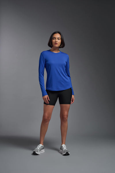A female model with short brown hair on a gray background, wearing the Women's Oxymesh™ Long Sleeve Tech Tee in the color royal blue from a full body front view. This shirt is made in the USA and is quick-drying and moisture-wicking. #color_royal-blue