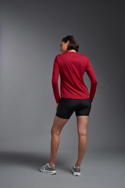 A female model with short brown hair on a gray background, wearing the Women's Oxymesh™ Long Sleeve Tech Tee in the color true red from a full body back view. This shirt is made in the USA and is quick-drying and moisture-wicking. #color_true-red