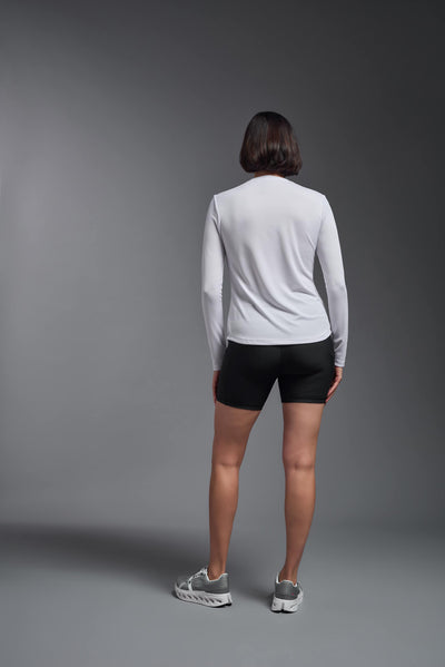 A female model with short brown hair on a gray background, wearing the Women's Oxymesh™ Long Sleeve Tech Tee in the color white from a full body back view. This shirt is made in the USA and is quick-drying and moisture-wicking. #color_white