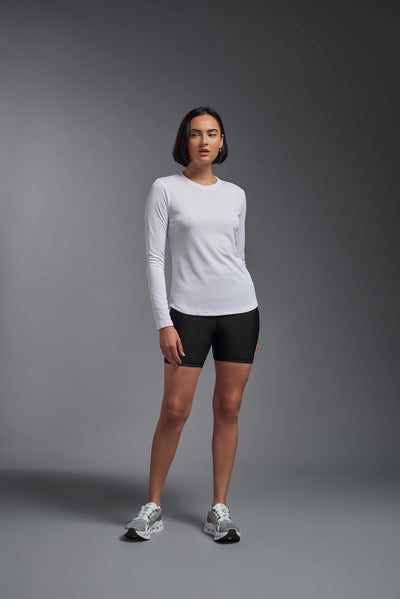 A female model with short brown hair on a gray background, wearing the Women's Oxymesh™ Long Sleeve Tech Tee in the color white from a full body front view. This shirt is made in the USA and is quick-drying and moisture-wicking. #color_white