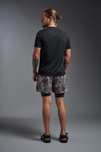 A blonde male model with a beard on a gray background, wearing the Men's Oxymesh™ Crewneck Tech Tee in the color black from a full body back view. This shirt is made in the USA and is quick-drying and moisture-wicking. #color_black