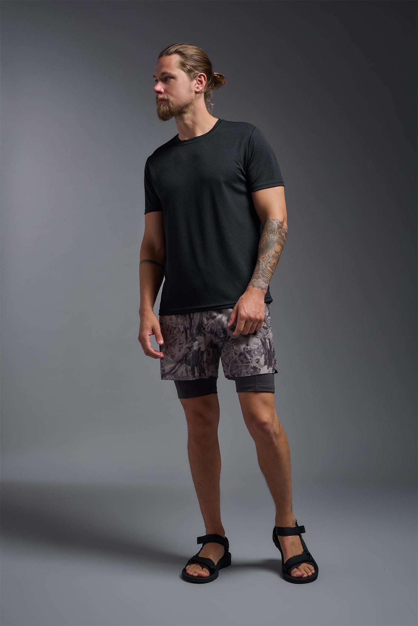 A blonde male model with a beard on a gray background, wearing the Men's Oxymesh™ Crewneck Tech Tee in the color black from a full body front view. This shirt is made in the USA and is quick-drying and moisture-wicking. #color_black