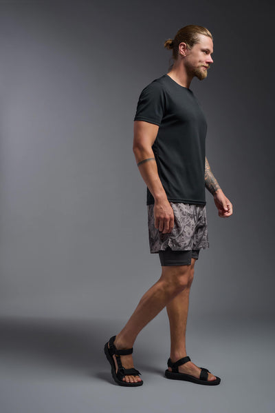 A blonde male model with a beard on a gray background, wearing the Men's Oxymesh™ Crewneck Tech Tee in the color black from a full body side view. This shirt is made in the USA and is quick-drying and moisture-wicking. #color_black